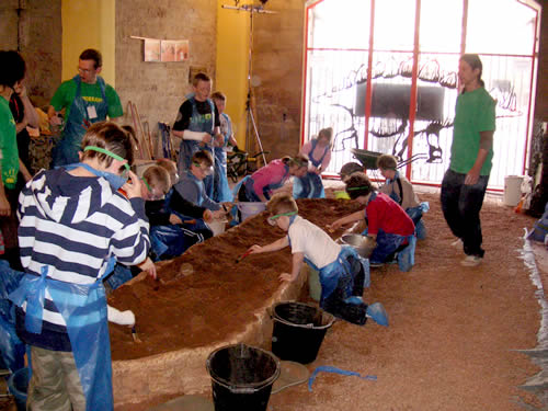 恐竜発掘ワークショップの風景。緑色のTシャツを着た大学生(アルバイト)の指示に従い、子どもたちが化石を「発掘」している。