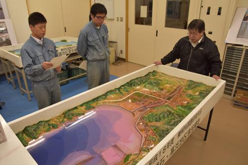 写真．山野目先生(右)の指導で、製作した津波模型を前に、実演会の練習をする生徒。