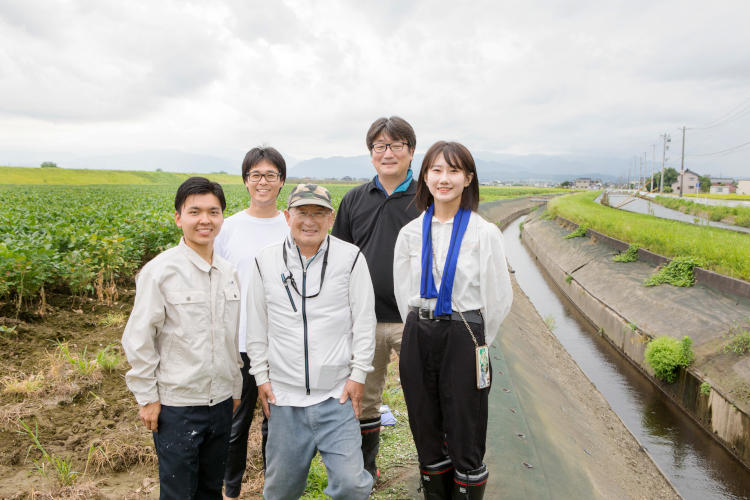 富山市婦中町で調査を行う乃田さん（後列右）らの研究チーム。中央は研究に協力している農家の小森さん