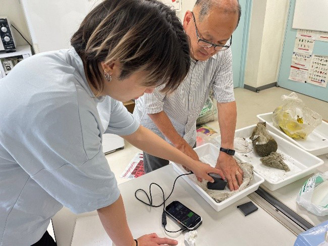プラスチックの種類を調べる機械を用いて底びき網の中のごみを調べる松下教授(写真右)と大学院生(長崎大学提供)